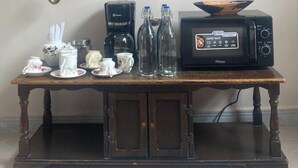 A kitchen with a coffee maker, two bottles, a microwave, and various kitchenware on a wooden table. - Hanaia House (Zanzibar Town)
