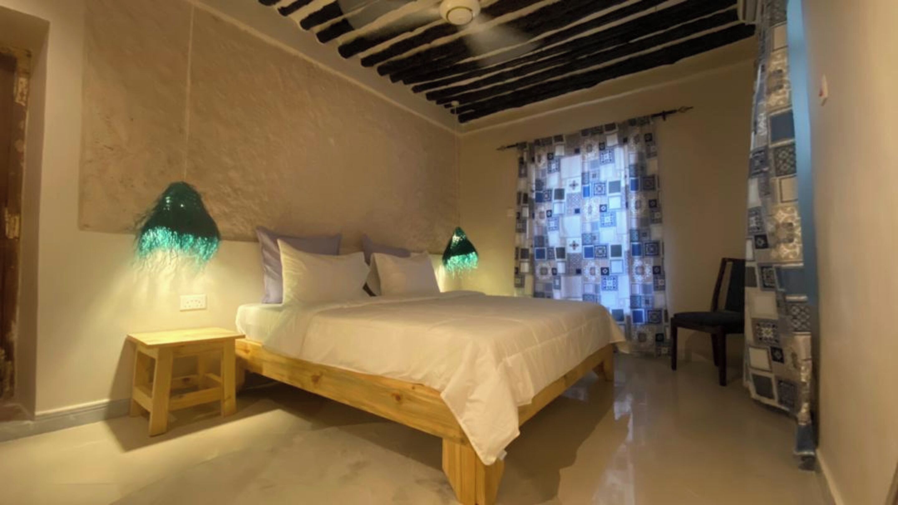 Ein Schlafzimmer mit einem hölzernen Bett, zwei Nachttischen, einem Deckenventilator und gemusterten Vorhängen.