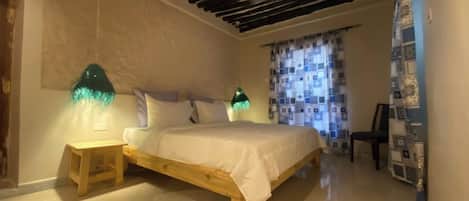 Un dormitorio con una cama de madera, dos mesitas de noche, un ventilador de techo y cortinas estampadas.