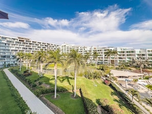 Un hotel moderno con varios pisos, un patio central con palmeras y una piscina.
