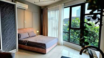 A modern bedroom with a bed, a desk, and a large window offering a city view.