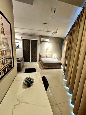 A modern bedroom with a bed, a desk with a plant, a large window, and a wall-mounted air conditioner. - Edumetro The New Duo (Subang Jaya)