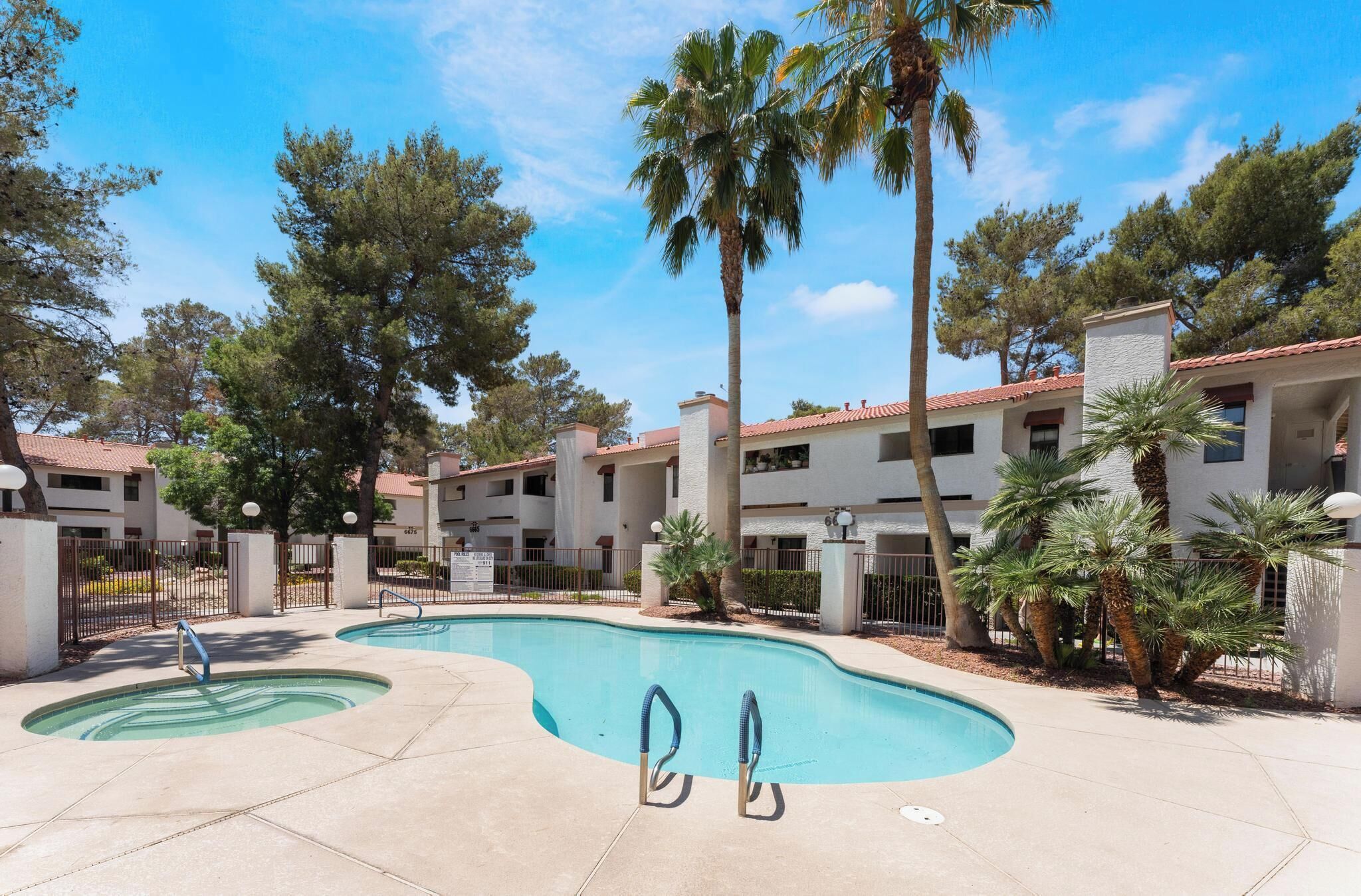 A swimming pool with two ladders, surrounded by palm trees and a multi-story building with balconies.