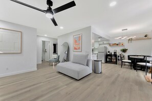 Ein modernes Wohnzimmer mit einem grauen Sofa, einem Essbereich mit Tisch und Stühlen sowie einer Küche im Hintergrund.
