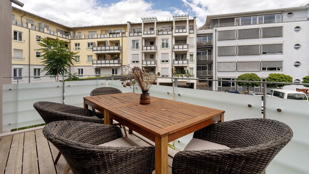 A rooftop terrace with wicker furniture, a wooden table, and a vase of dried flowers. - Holiday Apartment "Km Style 5" with Balcony & Wi-Fi (Freiburg im Breisgau)