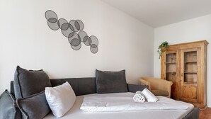 A neatly made bed with pillows, a grey sofa, a wooden cabinet, and a wall art piece. - Holiday Apartment "Km Style 5" with Balcony & Wi-Fi (Freiburg im Breisgau)