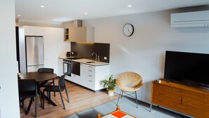 A modern kitchen with white cabinets, a stainless steel refrigerator, and a dining area with a table and chairs.
