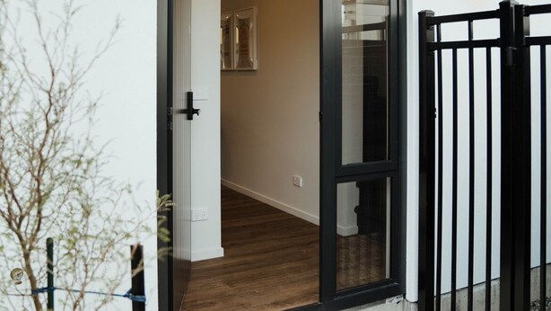 A modern building entrance with a glass door, a concrete step, and a black metal gate.