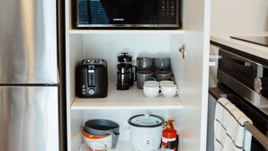 A compact kitchen with a stainless steel refrigerator, a microwave, a toaster, a coffee maker, and a fire extinguisher.