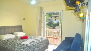 A bedroom with a bed, a sofa, a table, and a balcony with a view of buildings and greenery. - Holiday House Letta in a very quiet location Agios Gordios Beach (Agios Gordios)