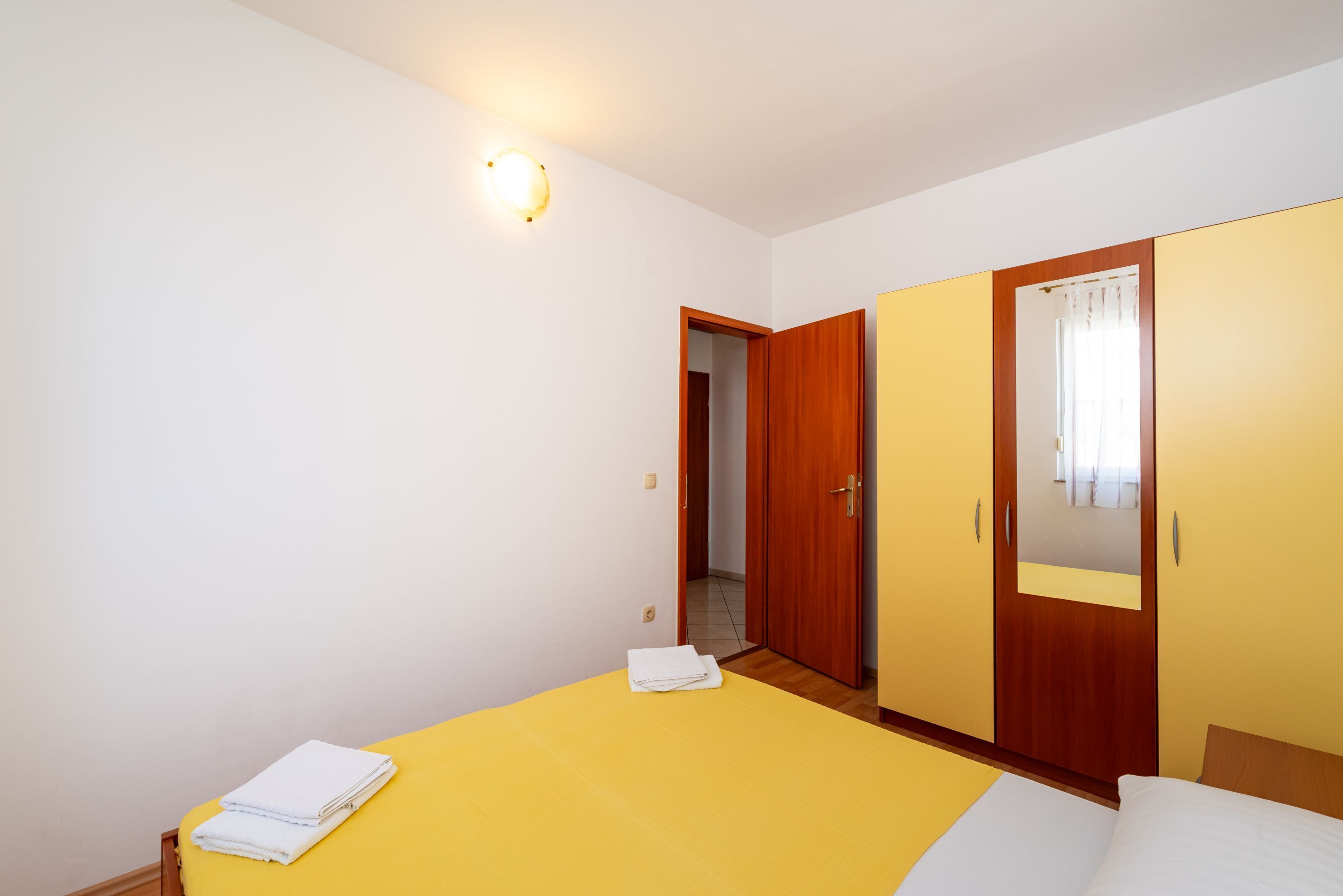 A bedroom with a bed, a wardrobe, a mirror, and a door leading to another room.