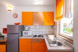 Keittiössä on oranssit kaapit, ruostumattomasta teräksestä valmistettu jääkaappi, mikroaaltouuni ja pesuallas.