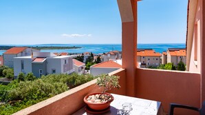 A balcony with a potted plant, a table, and a clear view of a coastal town. - Comfortable apartments Malina C6 br 8 (Novalja)