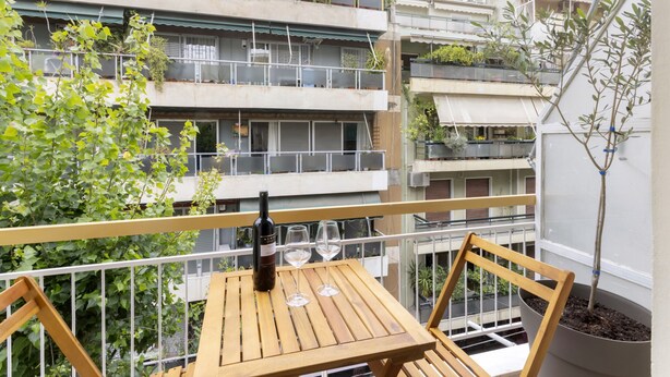 Un balcón con una mesa de madera, dos copas de vino y una botella.