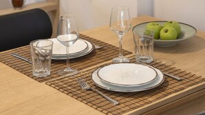 Una mesa de comedor dispuesta con platos, vasos y un bol de manzanas verdes.