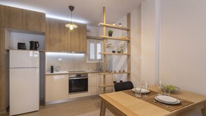 Una cocina moderna con armarios de madera, un refrigerador blanco, horno empotrado y una zona de comedor con una mesa de madera para dos personas.
