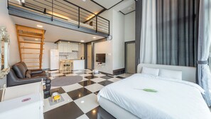 A hotel room with a checkered floor, a bed with white bedding, a desk with a chair, a kitchenette, and a balcony with a railing. - Gapyeong Chagall Spa Pension (Gapyeong)