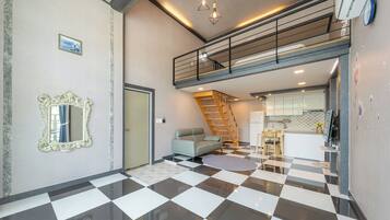 A spacious living area with a checkered floor, a sofa, a staircase, and a kitchen area.