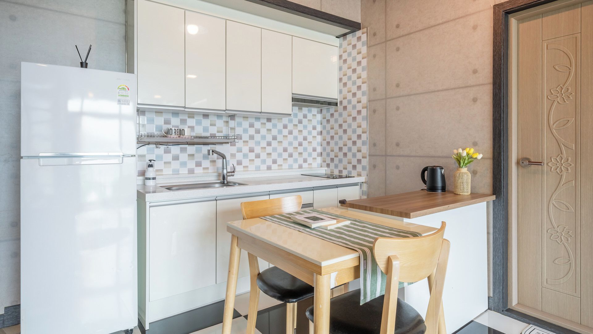 A compact kitchen with a refrigerator, sink, and a small dining area with a table and chairs.