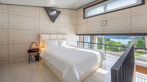 Ein modernes Schlafzimmer mit einem großen Bett, einem Nachttisch, einer Wandleuchte und einem Fenster mit Seeblick.