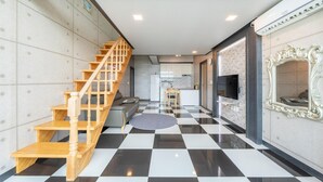 A modern interior with a checkered floor, a wooden staircase, a sofa, a dining area, and a TV mounted on the wall. - Gapyeong Chagall Spa Pension (Gapyeong)