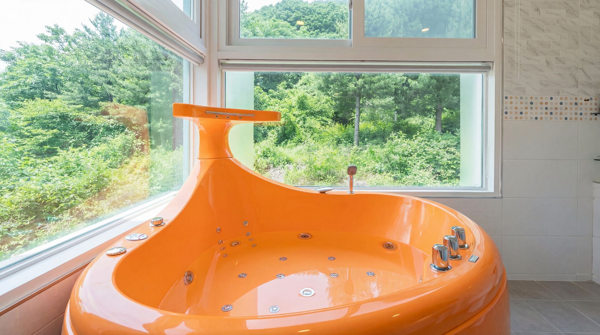 A modern bathroom with a large bathtub, a window with a forest view, and a tiled wall.