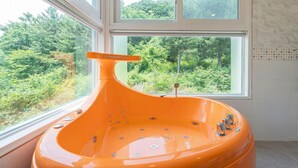 Un baño moderno con una bañera grande, una ventana con vistas a un bosque y un muro con azulejos.