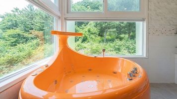 Un baño moderno con una bañera grande, una ventana con vistas a un bosque y un muro con azulejos.