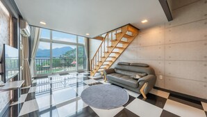 A modern living room with a grey sofa, a round rug, and a staircase with wooden railings. - Gapyeong Chagall Spa Pension (Gapyeong)