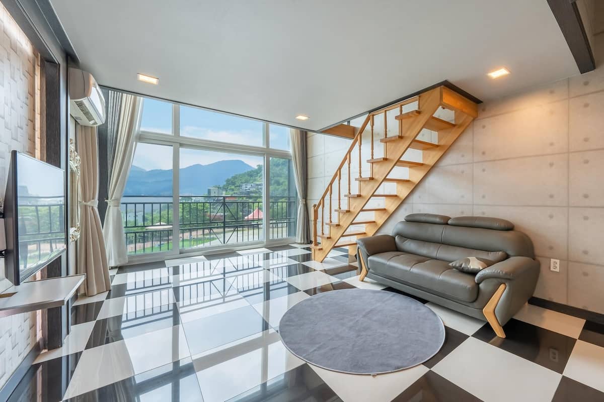 Ein modernes Wohnzimmer mit einem grauen Sofa, einem runden Teppich und einer Treppe mit Holzläufer.