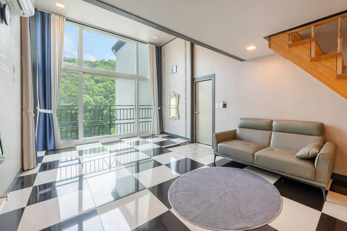 Ein modernes Wohnzimmer mit einem Schachbrettmuster-Boden, einem grauen Sofa und einem großen Fenster mit Balkon.