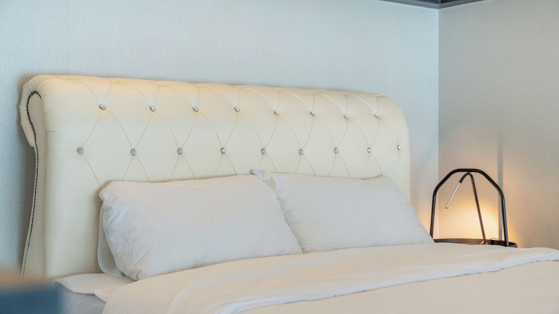 A bed with a tufted headboard, two pillows, and a bedside lamp.