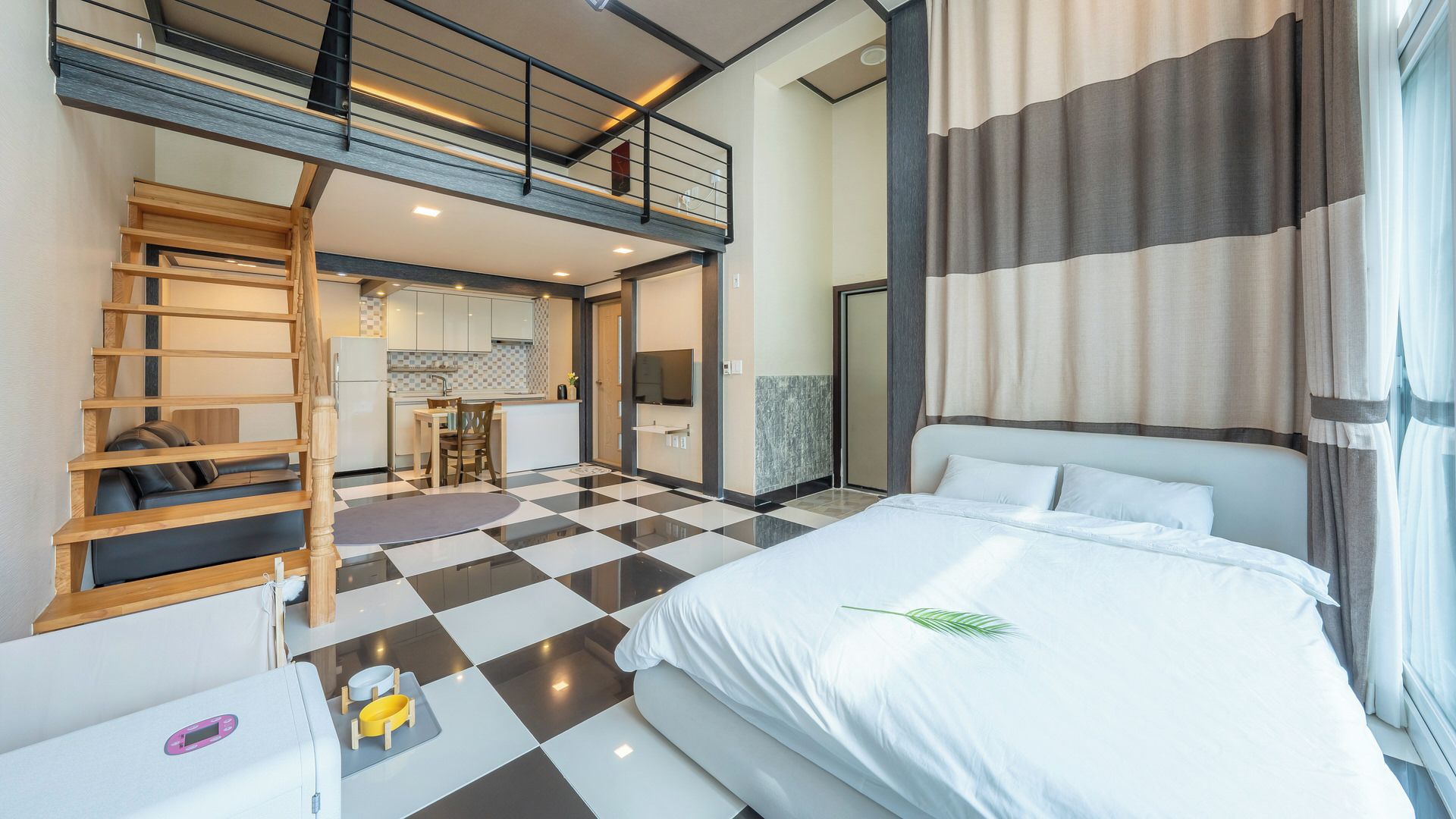 A hotel room with a bed, a desk, a chair, a sofa, a dining area, and a staircase.
