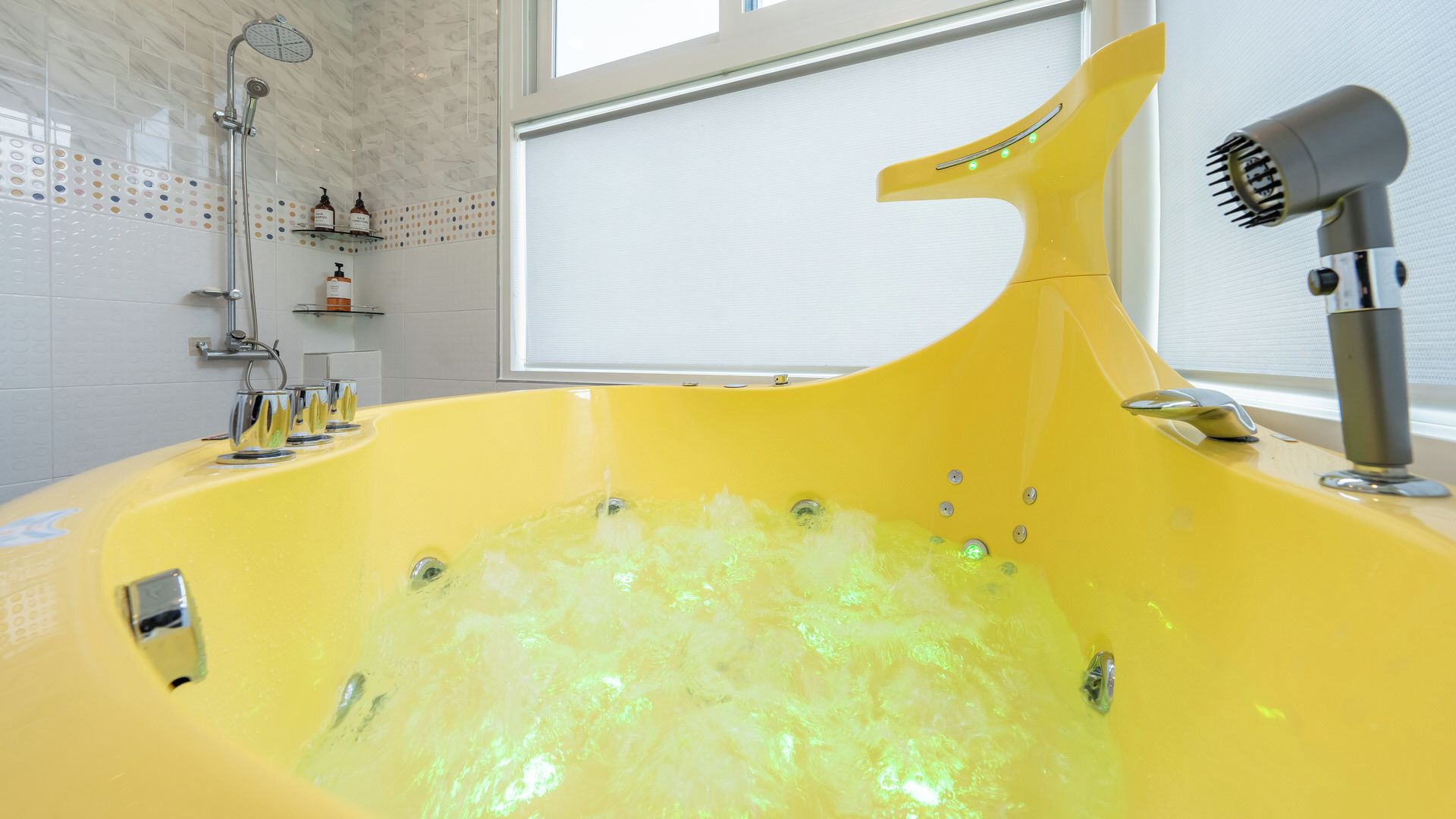 A yellow bathtub with bubbles, a showerhead, and a hairdryer.