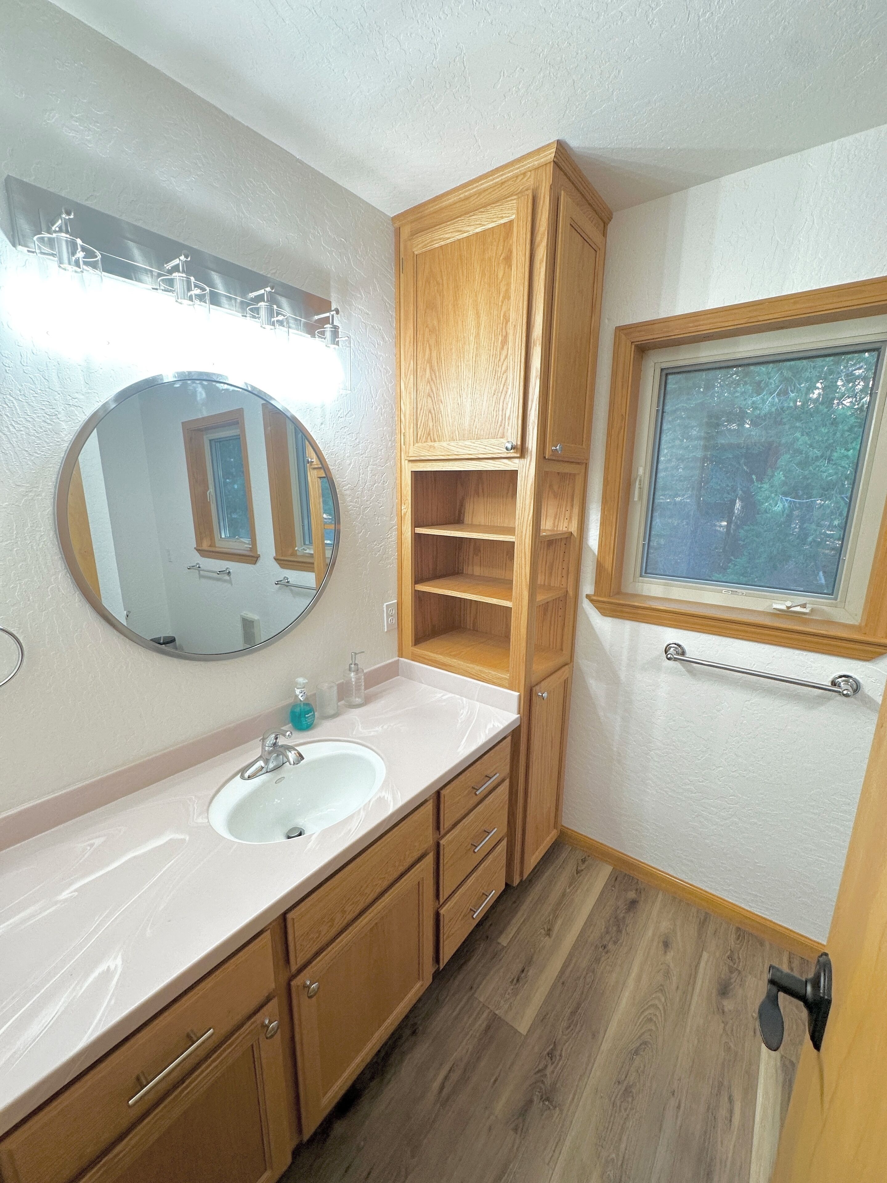 A bathroom with a white sink, wooden cabinets, a mirror, and a window.
