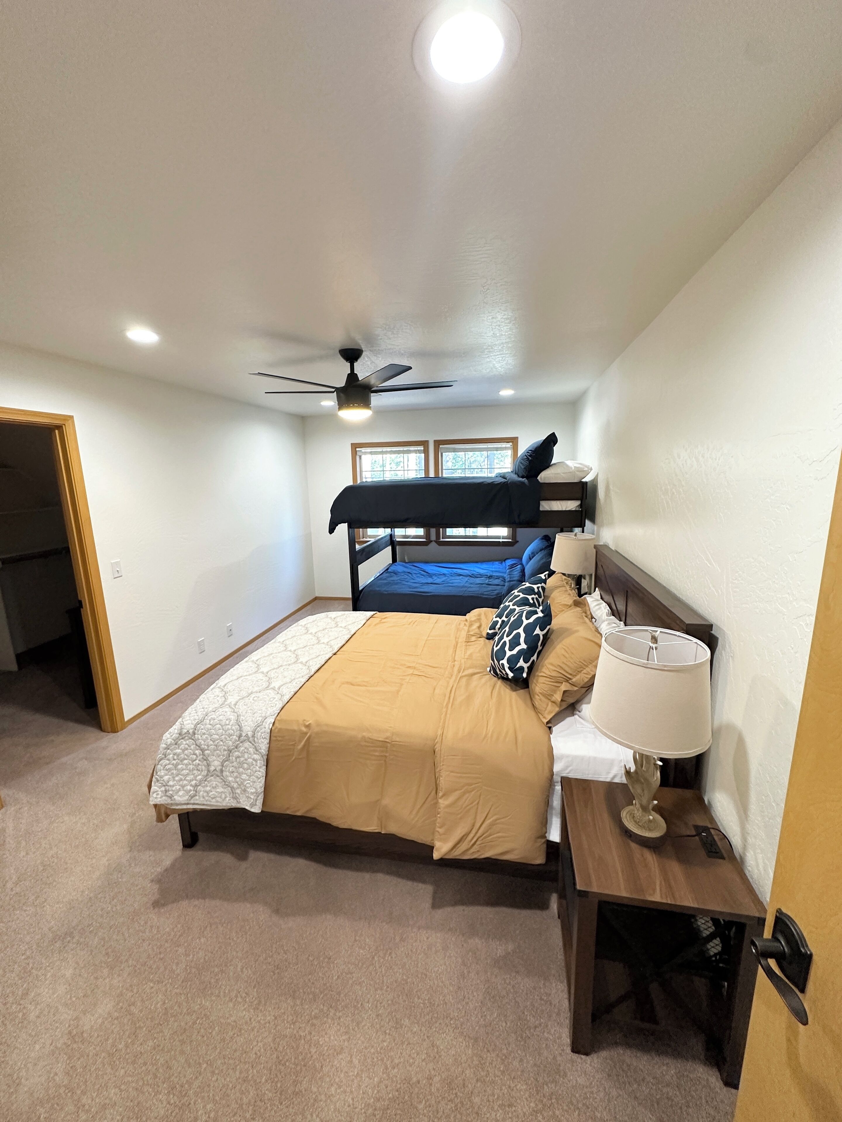 Une chambre avec un lit superposé, une table de chevet avec une lampe et un ventilateur de plafond.