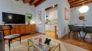 Een woonkamer met een flatscreen-tv, een glazen salontafel, een bank en een eethoek met stoelen.