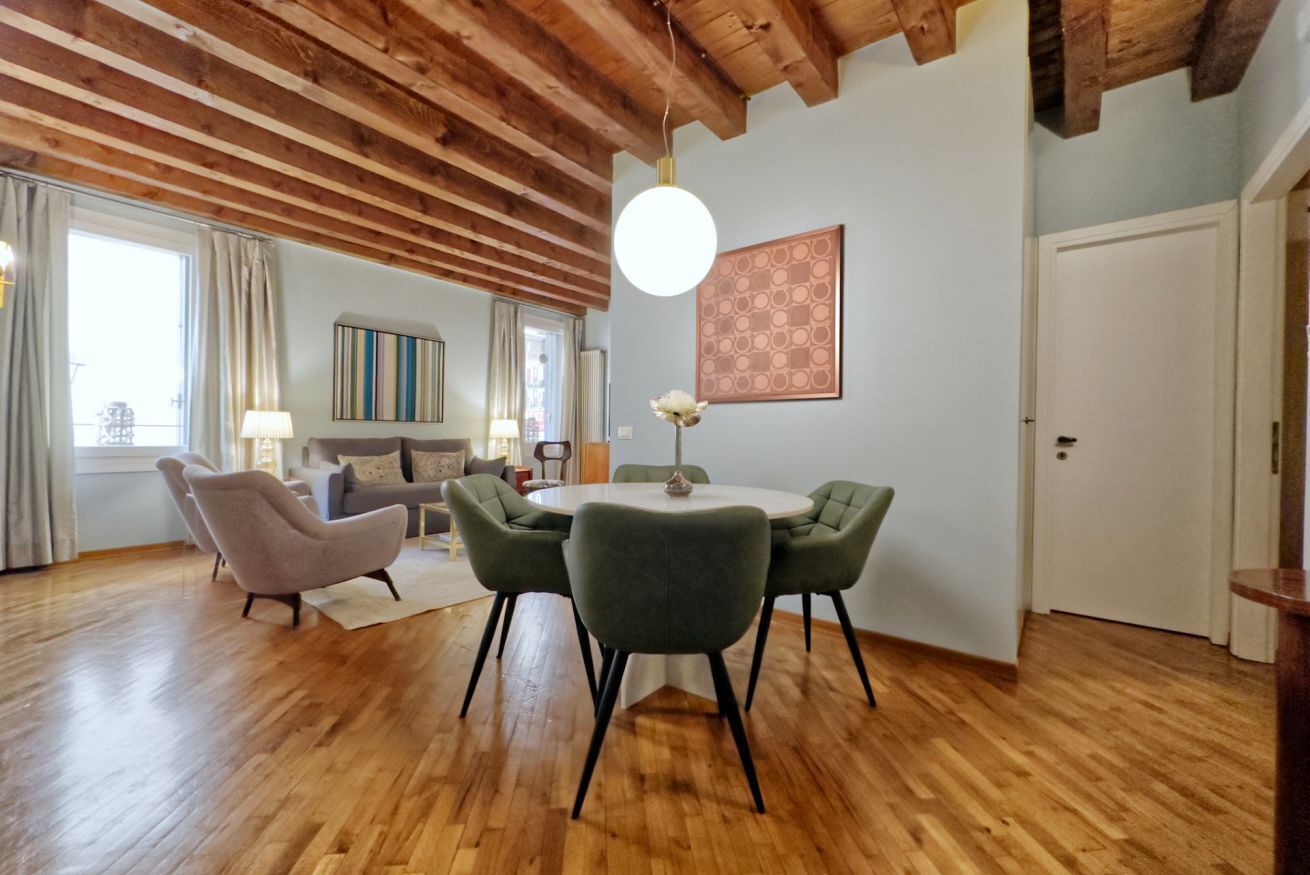 Une pièce avec un plancher en bois, une table ronde entourée de chaises, un canapé, une lampe et un tableau accroché au mur.