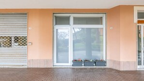 Entrada de un edificio con un gran ventanal, una reja metálica y macetas con flores.