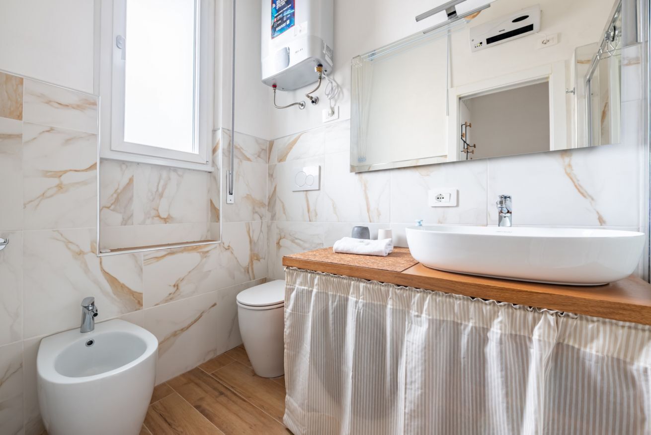 Une salle de bain avec un mur en marbre, un meuble-lavabo en bois, un grand lavabo, un bidet et des toilettes.