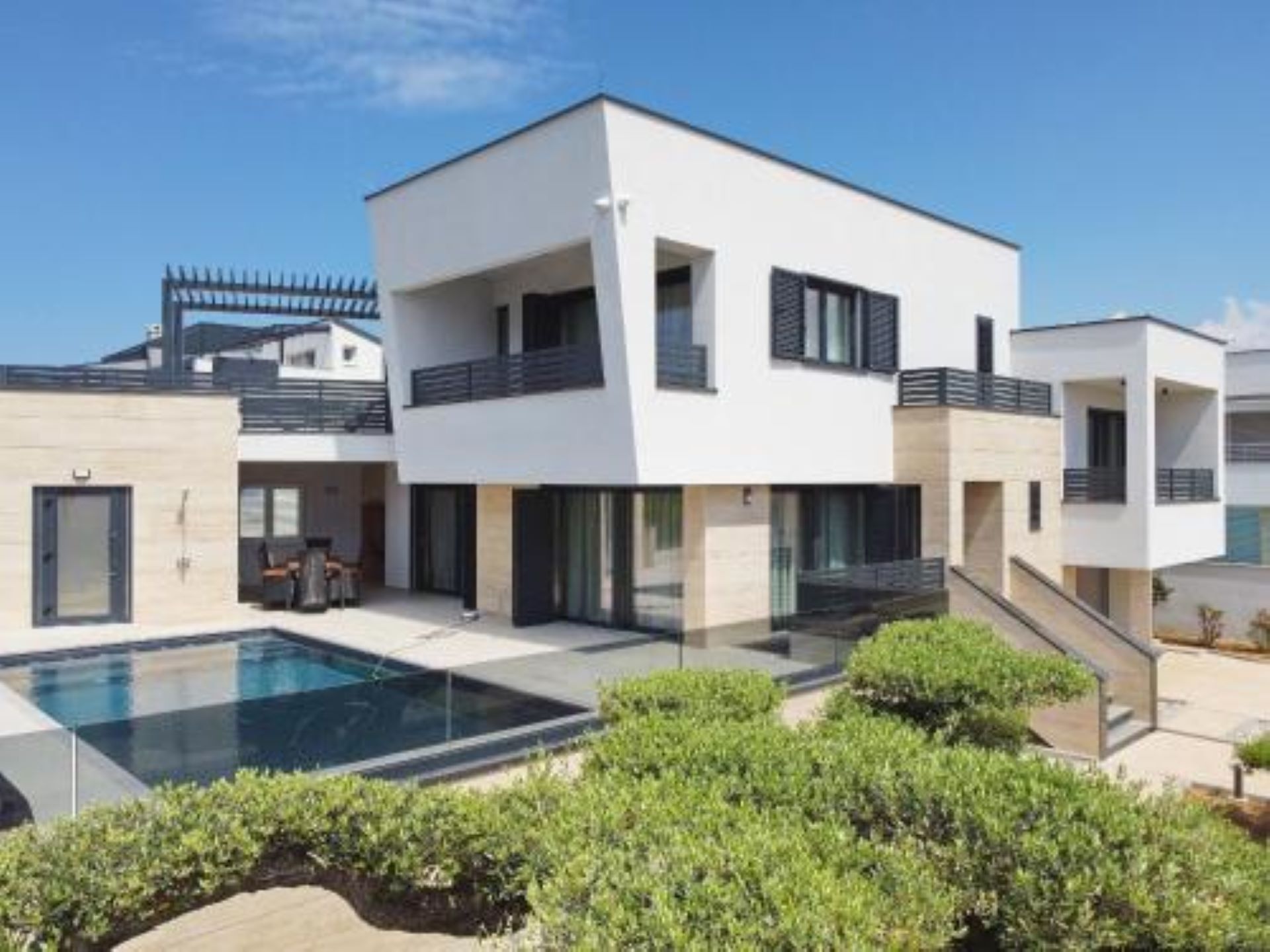 Una casa moderna de dos pisos con piscina, un porche cubierto y un jardín bien cuidado.