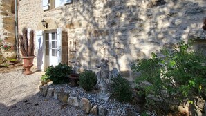 A stone building with a gravel driveway, a potted plant, and a metal birdcage. - Charm and serenity... (Parisot)
