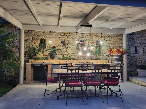 An outdoor patio with a stone wall, wooden ceiling, and a dining table with chairs. - Charm and tranquility... (Parisot)