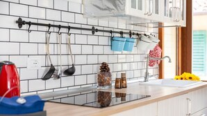 Een keuken met een zwart aanrecht, witte kasten, een hangrek met keukengerei en een raam met groene luiken.