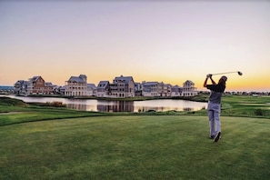 A golf course with a water body and buildings in the background. - Stunning designer home- next to beach with access to two resort pools (Port Aransas)
