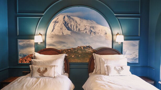 Un dormitorio con dos camas, un mural de una montaña y una pared azul.