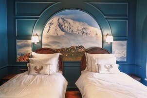 Un dormitorio con dos camas, un mural de una montaña y una pared azul.