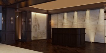 Un vestíbulo moderno con paneles de madera oscura, una pared de mármol con diseño de paisaje urbano y un mostrador de recepción central de madera oscura.
