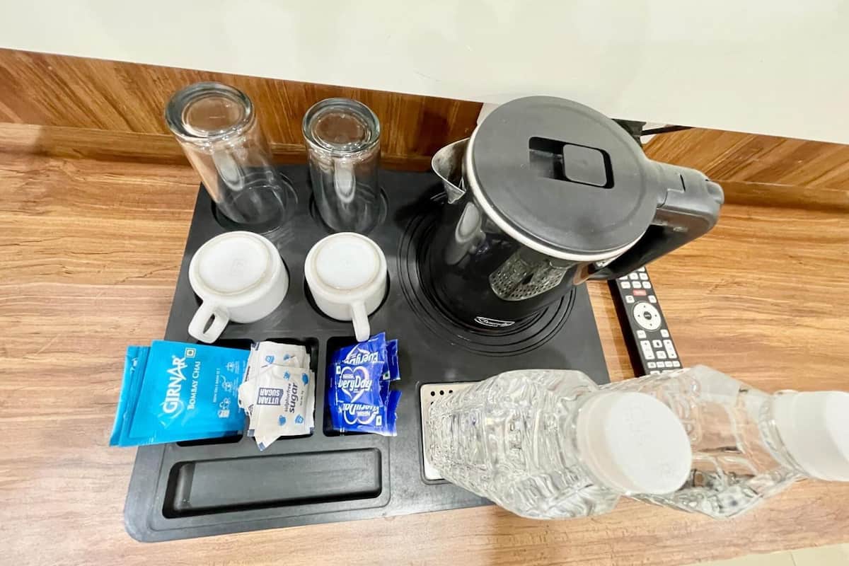 A coffee maker, two cups, sugar packets, a water bottle, and a remote control on a wooden countertop.