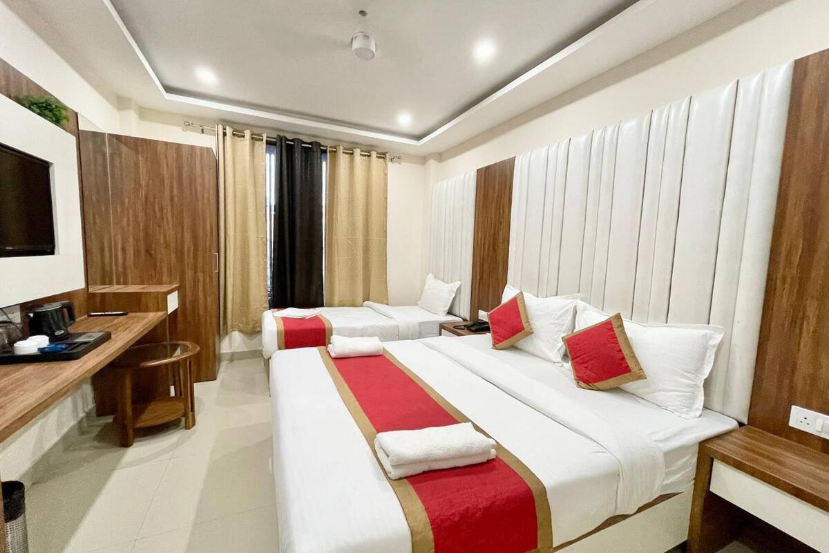 A hotel room with two beds, a desk, a TV, and a window with curtains.